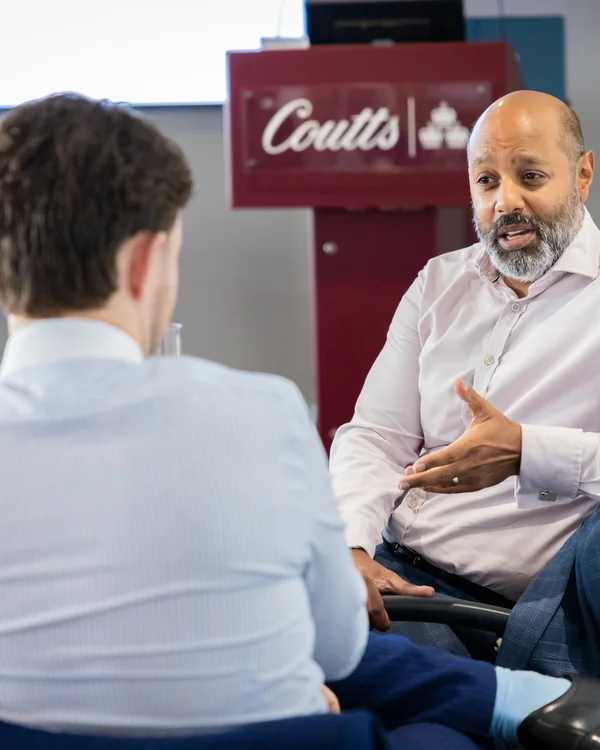 Two people in conversation at a Coutts training session, one leaning forward attentively.